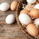 white and brown eggs laying in a brown basket filled with straw.